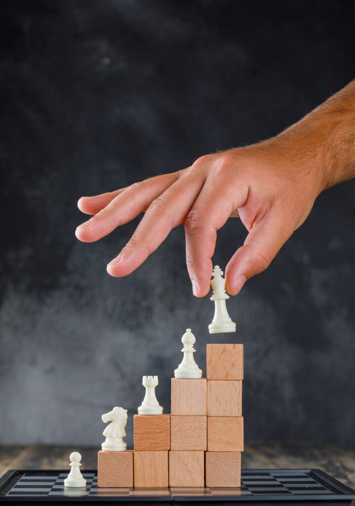 business success concept with chessboard on wooden and foggy background side view. man placing figure on pyramid of blocks.